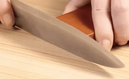 User sharpening a knife by sliding it through the Magnetic Rolling Knife Sharpener on a wooden surface