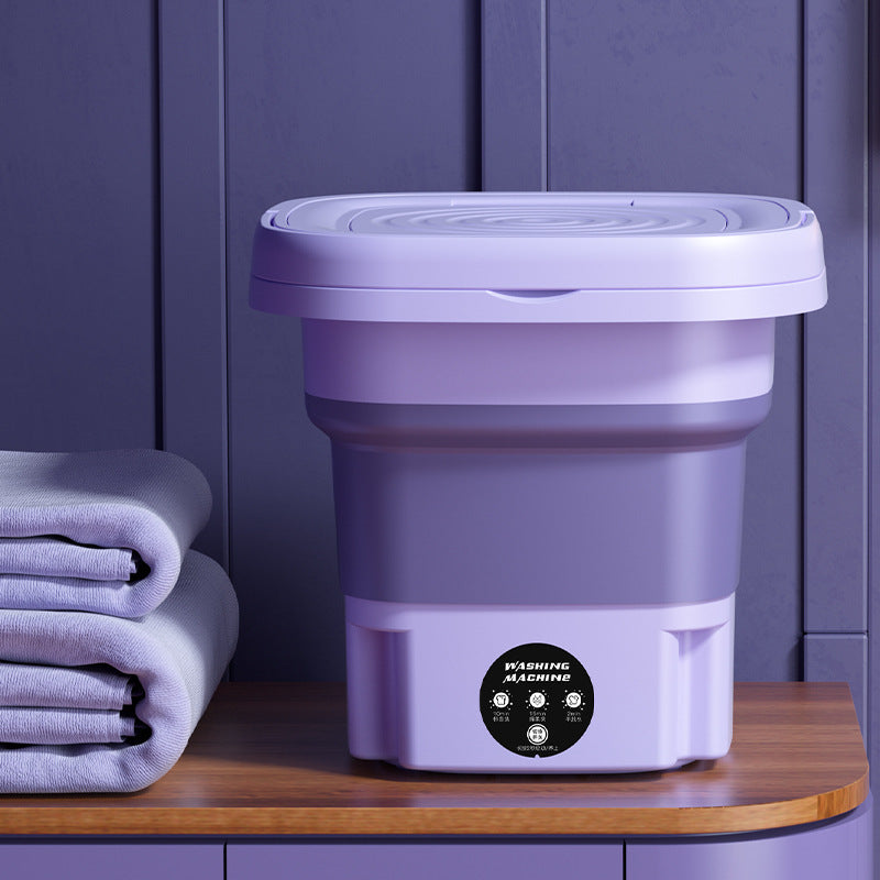 Foldable washing machine in purple color variant on wooden surface with towels